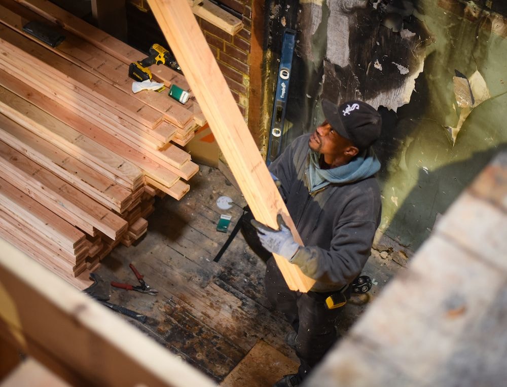 A construction worker lifts a 2x4 from a stack