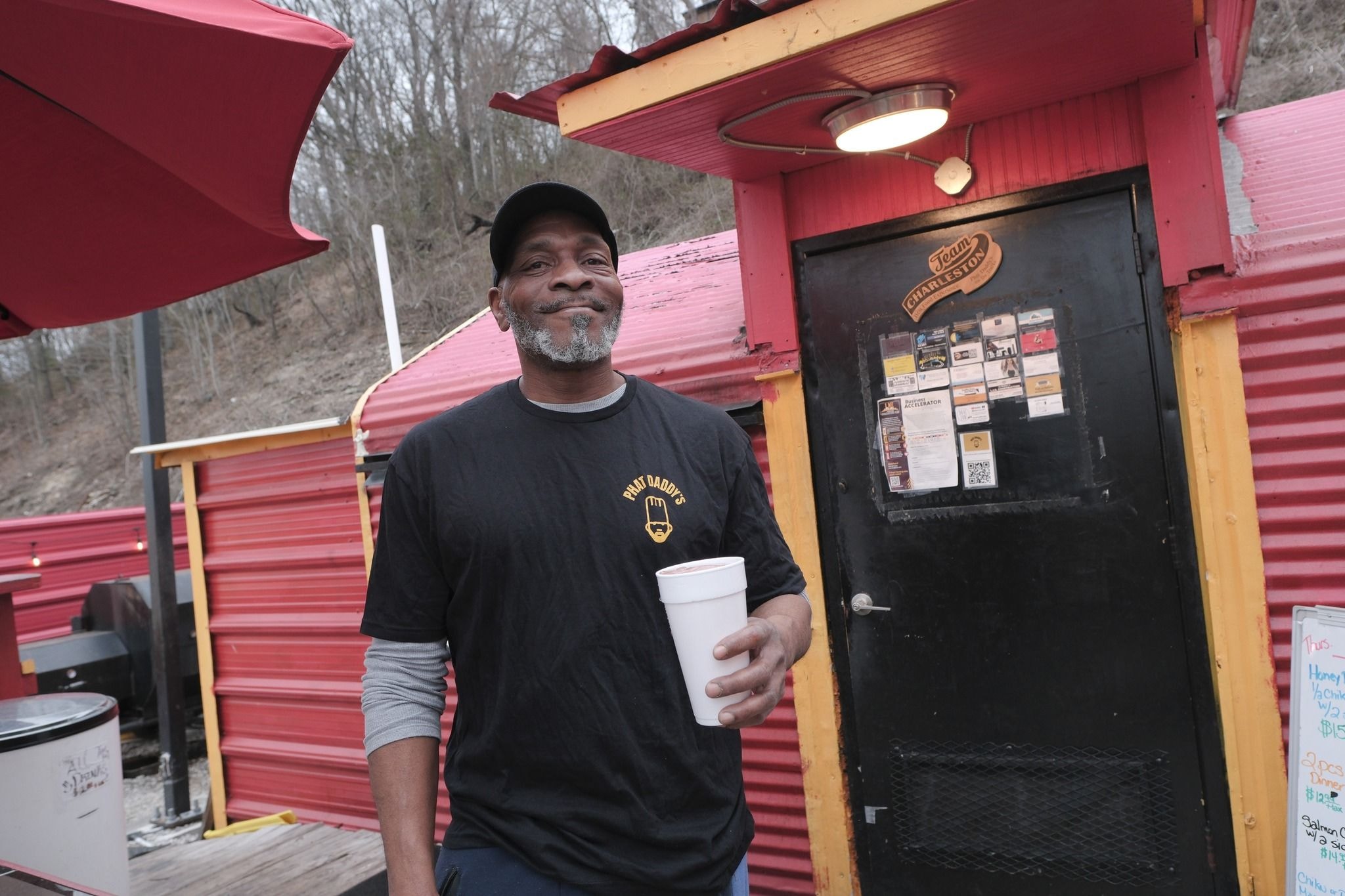 A man in a Phat Daddy's shirt stands on the red-colored deck of a BBQ stand