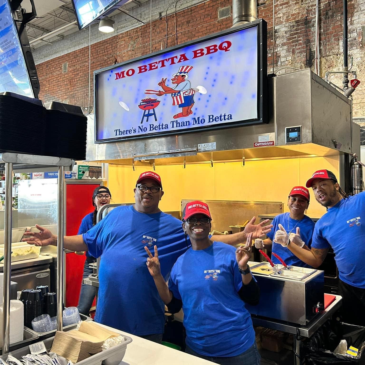 Workers in blue shirts at a BBQ stand in an indoor market