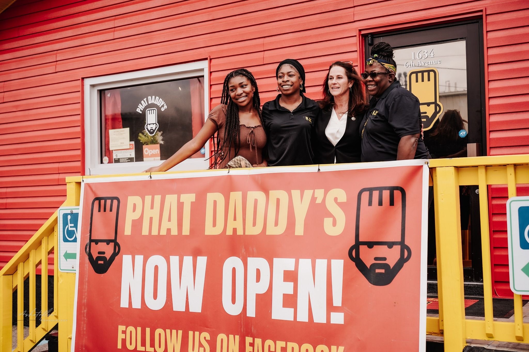 People on a porch of a red building with a banner that says "Phat Daddy's Now Open!"