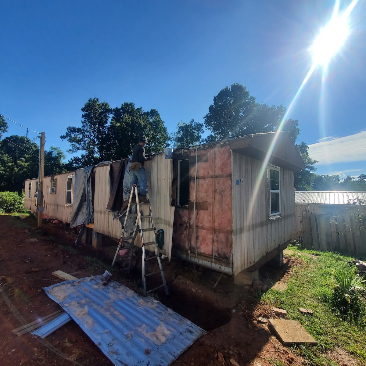 Workers from Chispas pulling off the exterior sheathing of a trailer under a bright blue sky, revealing inadequate insulation underneath.