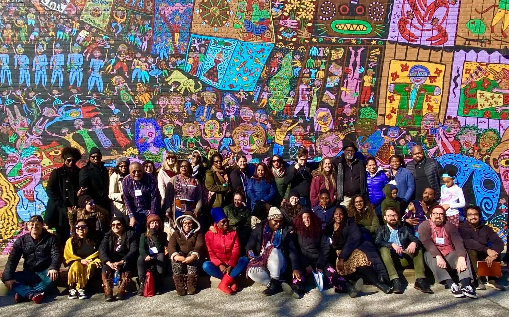 A large group of people gathered under a colorfully painted wall