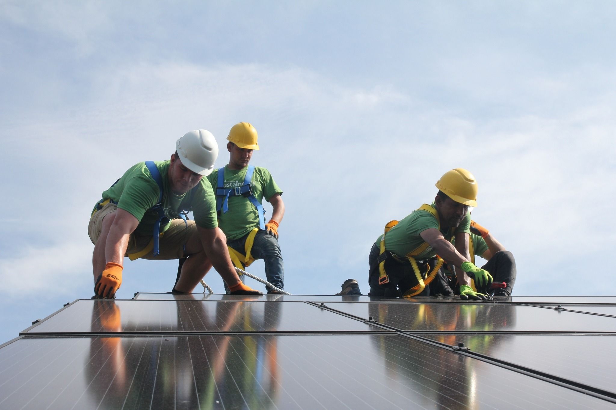 Three workers installing solar panels on a roof