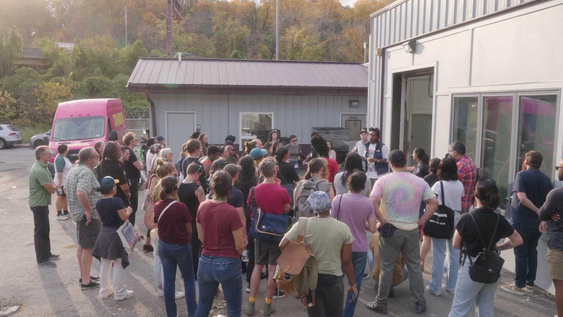 People gathered outside a factory, listening to a worker-owner talk about their business